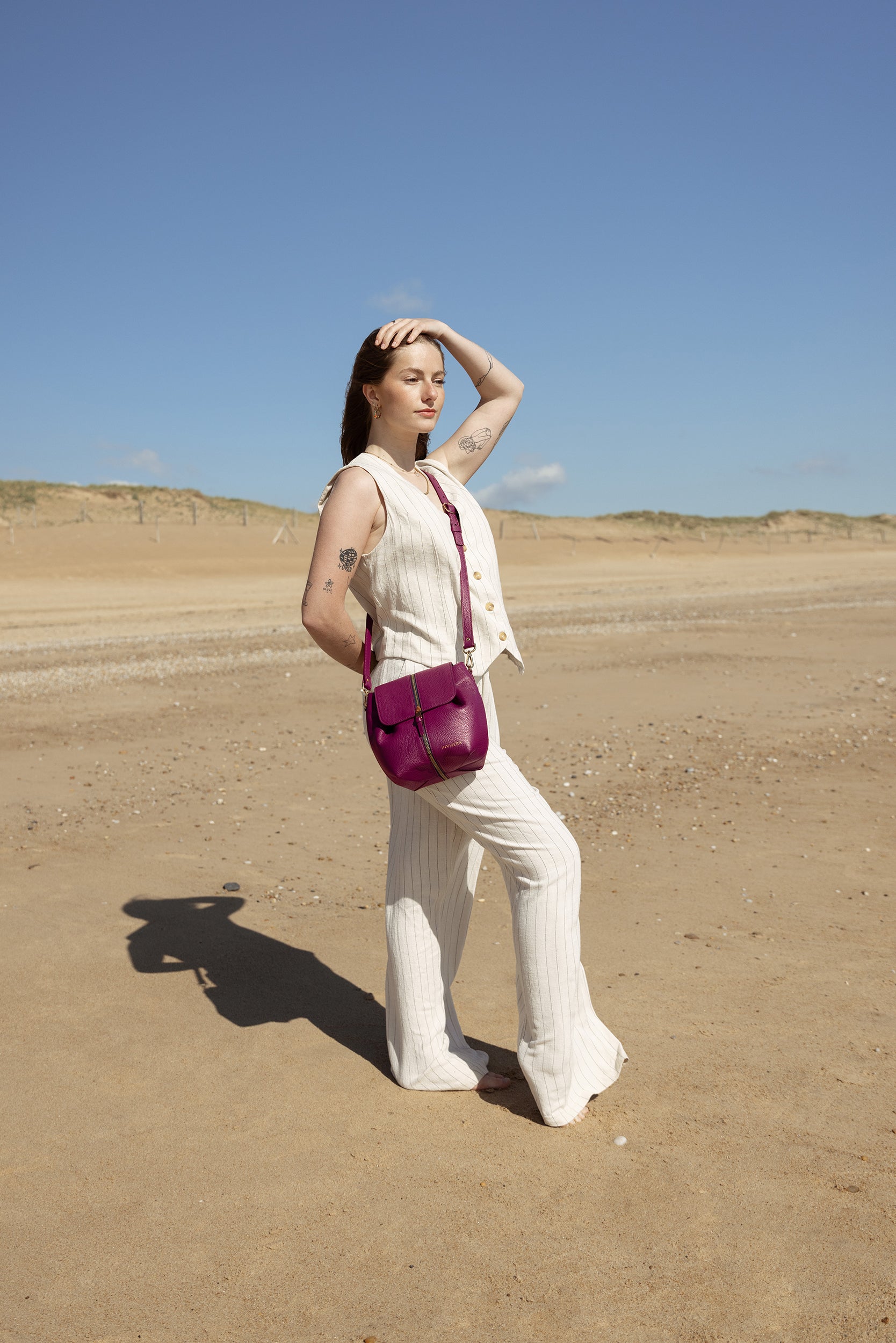 Une femme libre connectée à la nature des plages vendéennes, portant un sac à main cuir rose italien porté bandoulière amovible. Son look allure élégante vêtue d'un ensemble blanc à rayures noires.