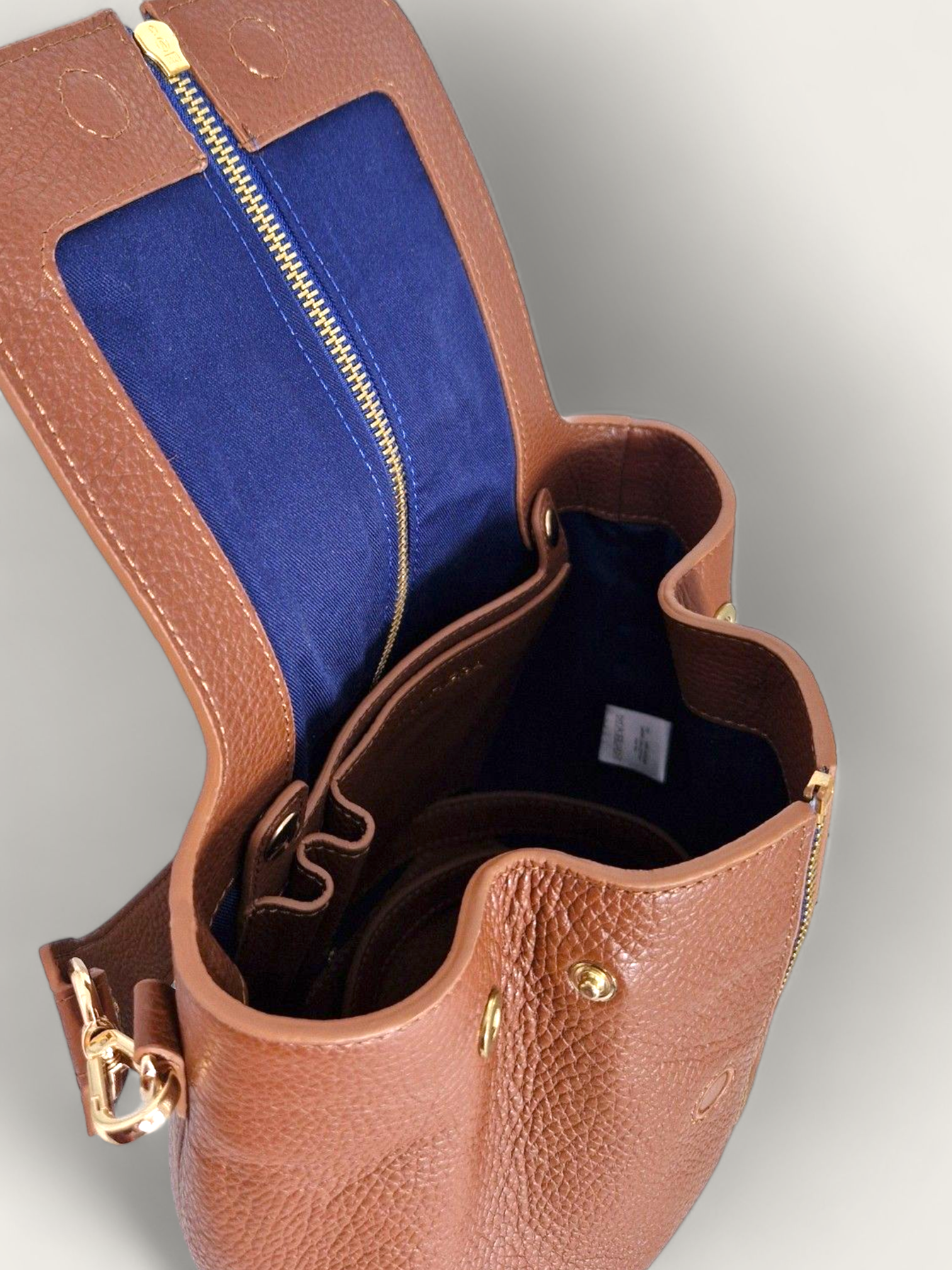 Aperçu de l'intérieur du sac cuir marron avec doublure de coton couleur bleu nuit et zip central, fermeture aimentée pour y mettre vos essentiels. Sur le côté du sac à main en cuir, des pressions pour une ouverture plus grande. A l'intérieur se trouve une poche amovible avec compartiment stylo.