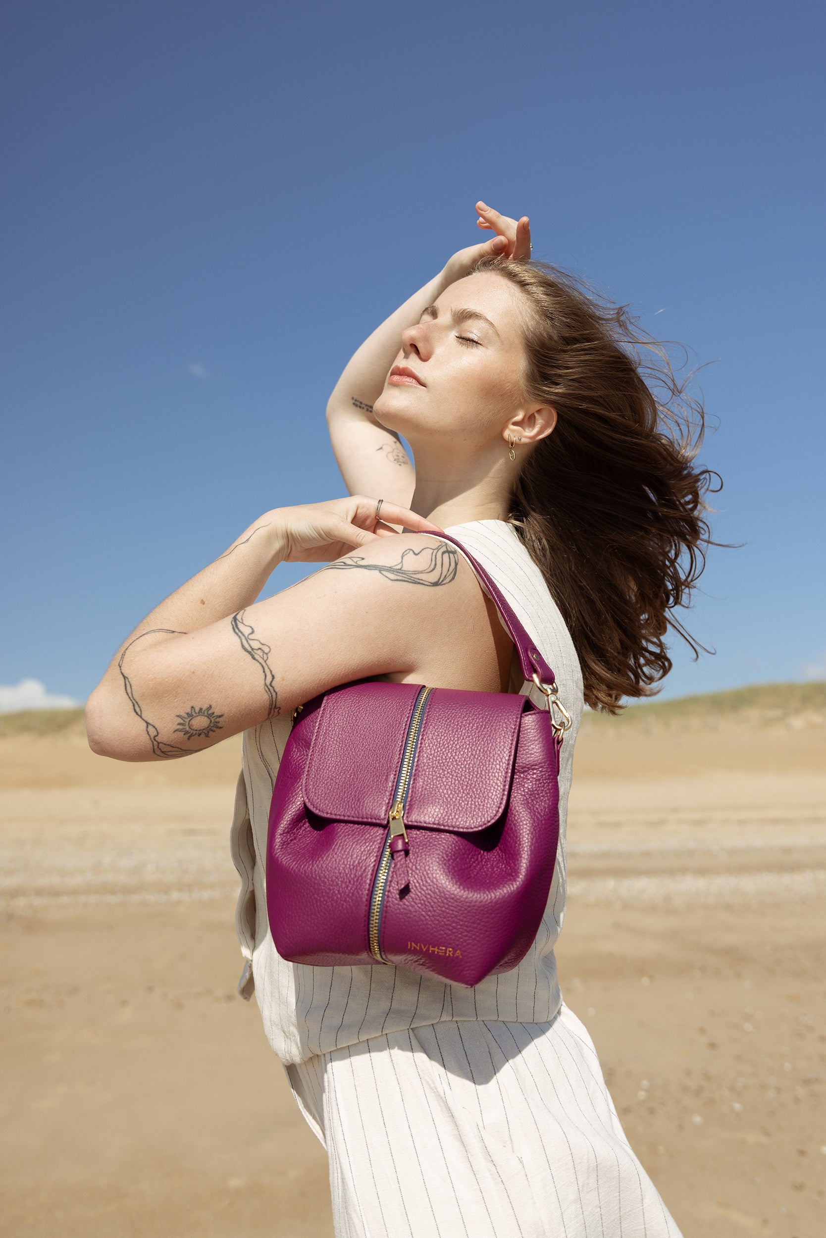 Femme libre et audacieuse portant un sac à main rose porté épaule doté d'une fermeture au milieu; Pièce conçue par INVHERA au coeur des plages vendéennes.