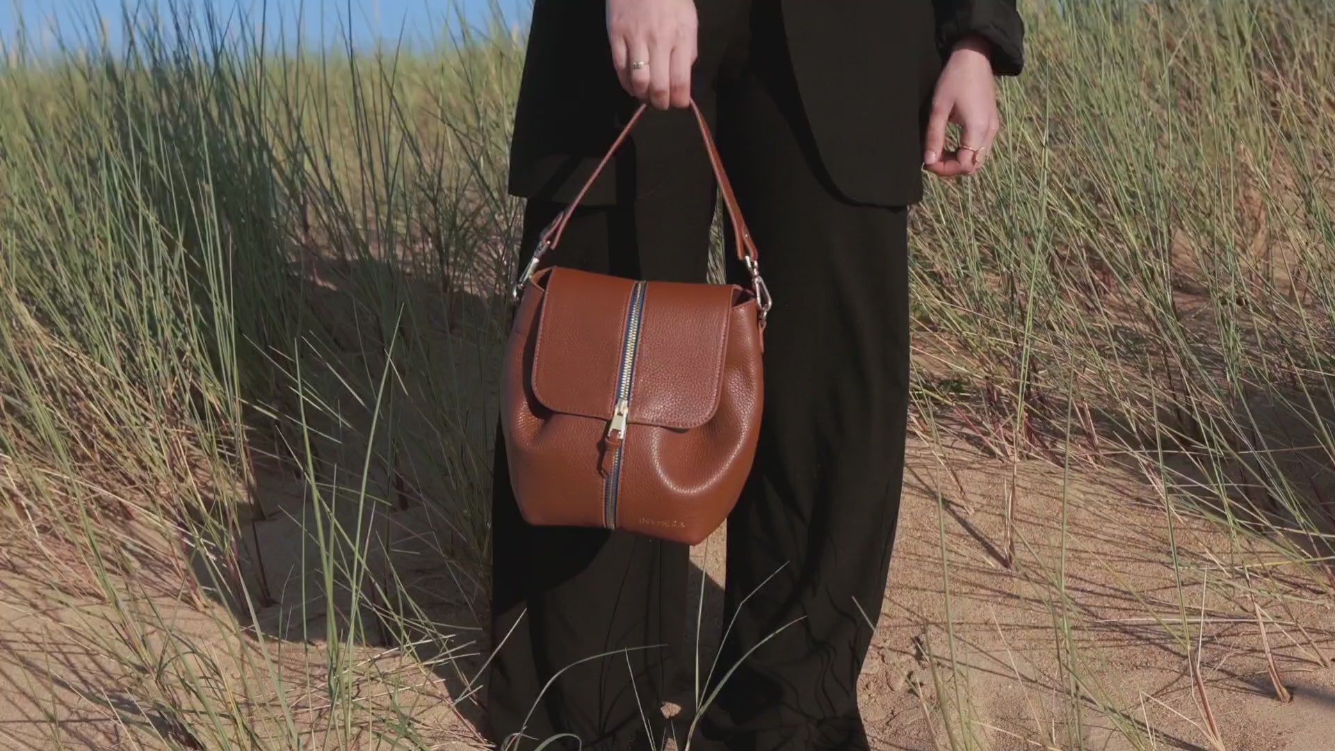 Un sac à main cuir marron porté main de chez INVHERA se balançant au main d'une femme indépendante, vidéo, montrant le changement de style, et de couleur grâce à notre système astucieux. De façon unicolore ou bicolore.