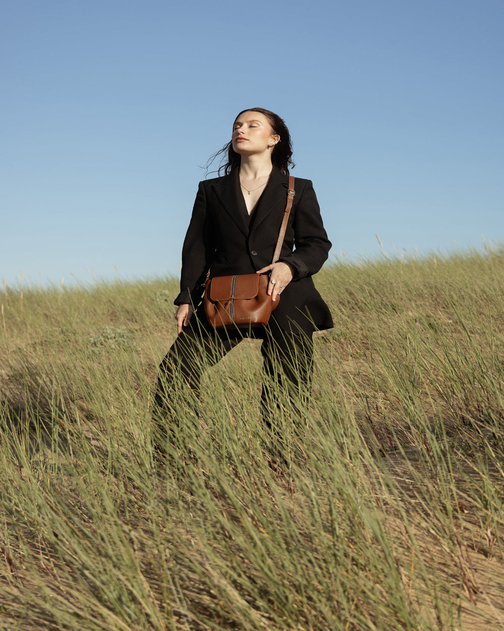Une femme libre connectée à la nature, portant un sac à main cuir marron italien porté bandoulière amovible. Son look allure élégante vêtue d'un ensemble blazer noir.