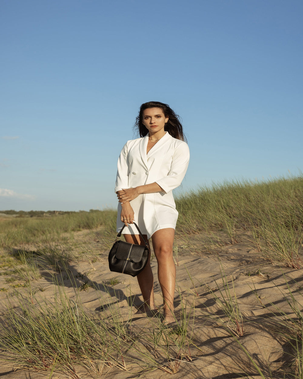 Sac à main noir porté main par une femme indépendante vêtue d'une robe blazer blanche. L'originalité fait toute la différente avec nos pièces interchangeables.